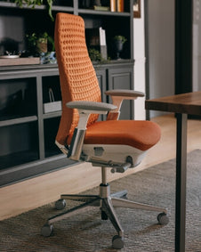 An orange Haworth Fern office chair in front of a desk.