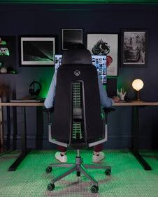 A man sitting in the Haworth x Xbox: Fern Gaming chair in a room with green LED lights.