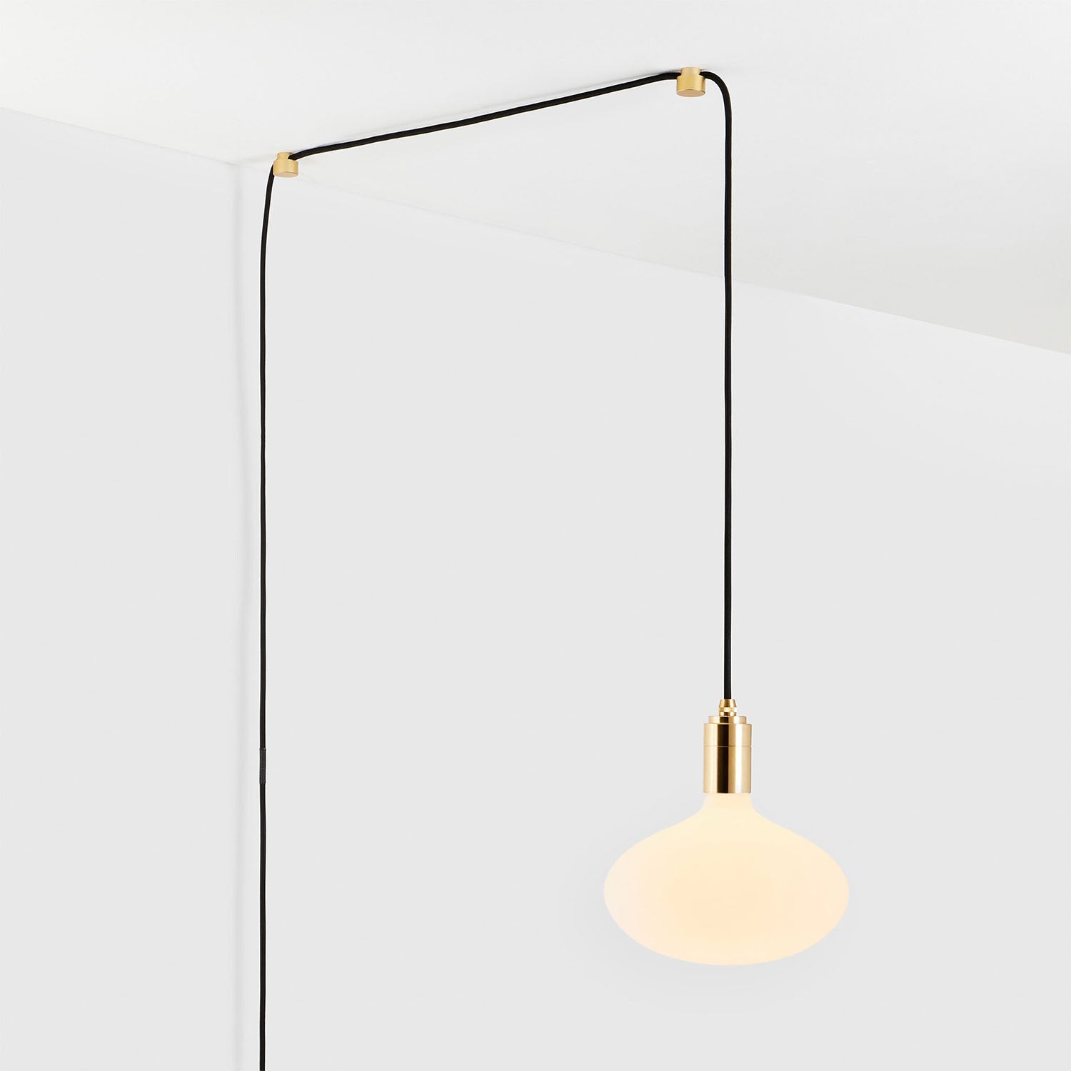 Modern minimalist pendant light with gold fixture and black cord hanging from the ceiling, illuminating white background.