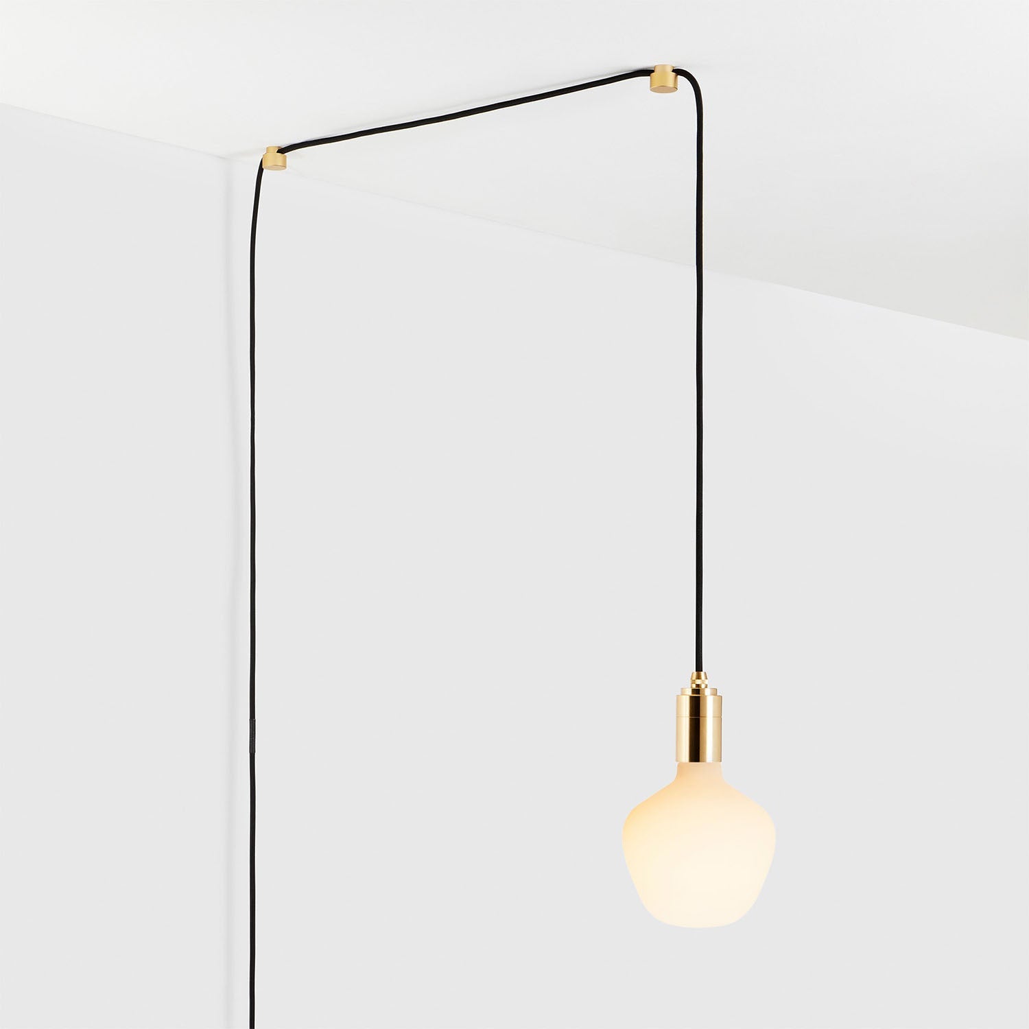 Modern ceiling-hung pendant light bulb with gold fixture and black cord against a white background.