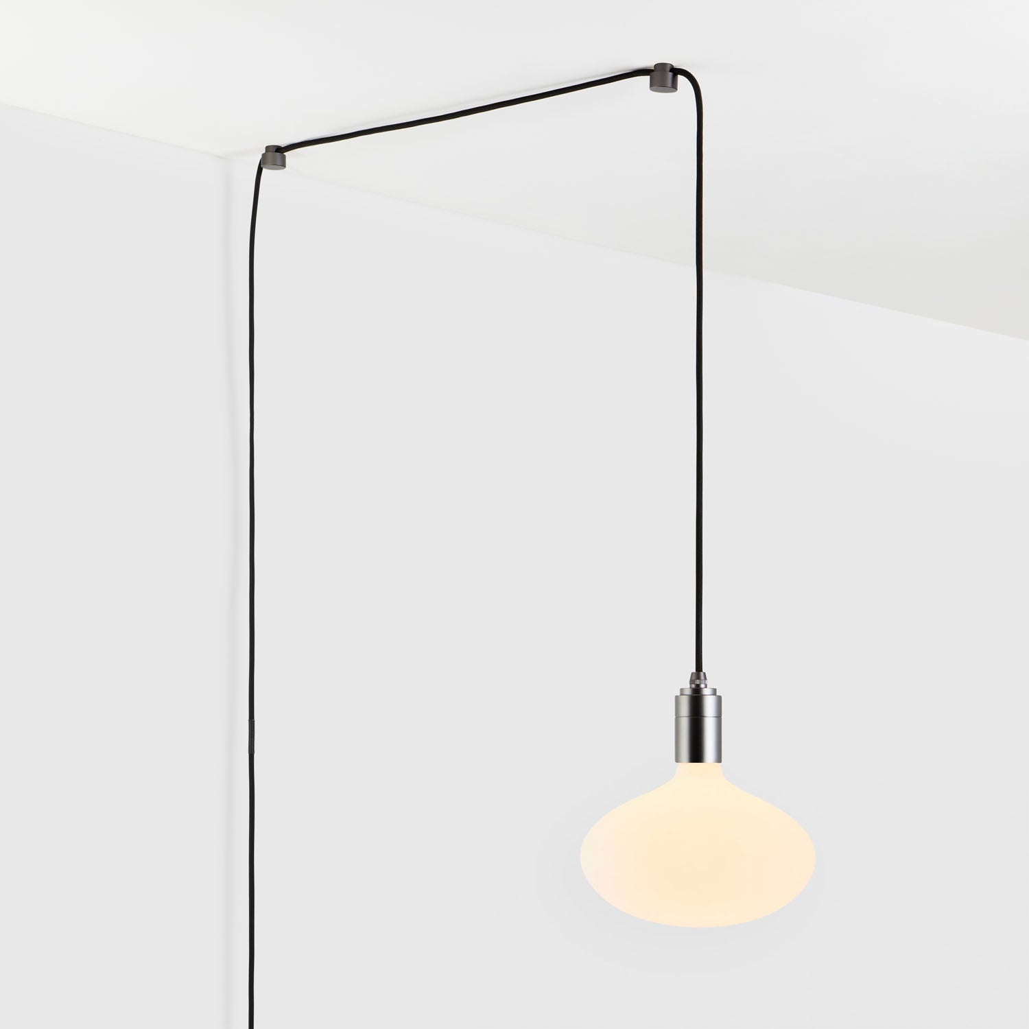 Modern hanging pendant light with black cord against white ceiling and wall.