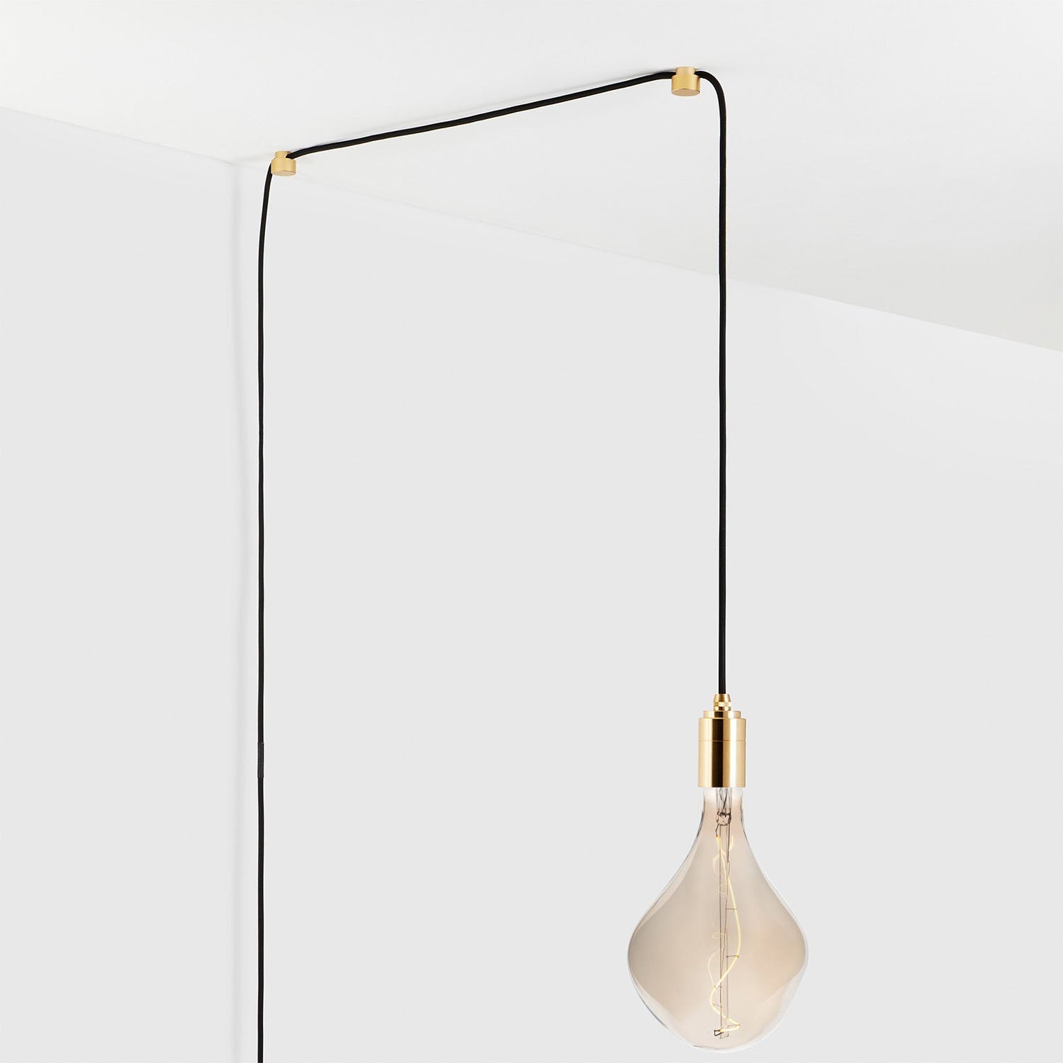 Modern minimalist light bulb pendant with gold fixture and black cord hanging from ceiling.