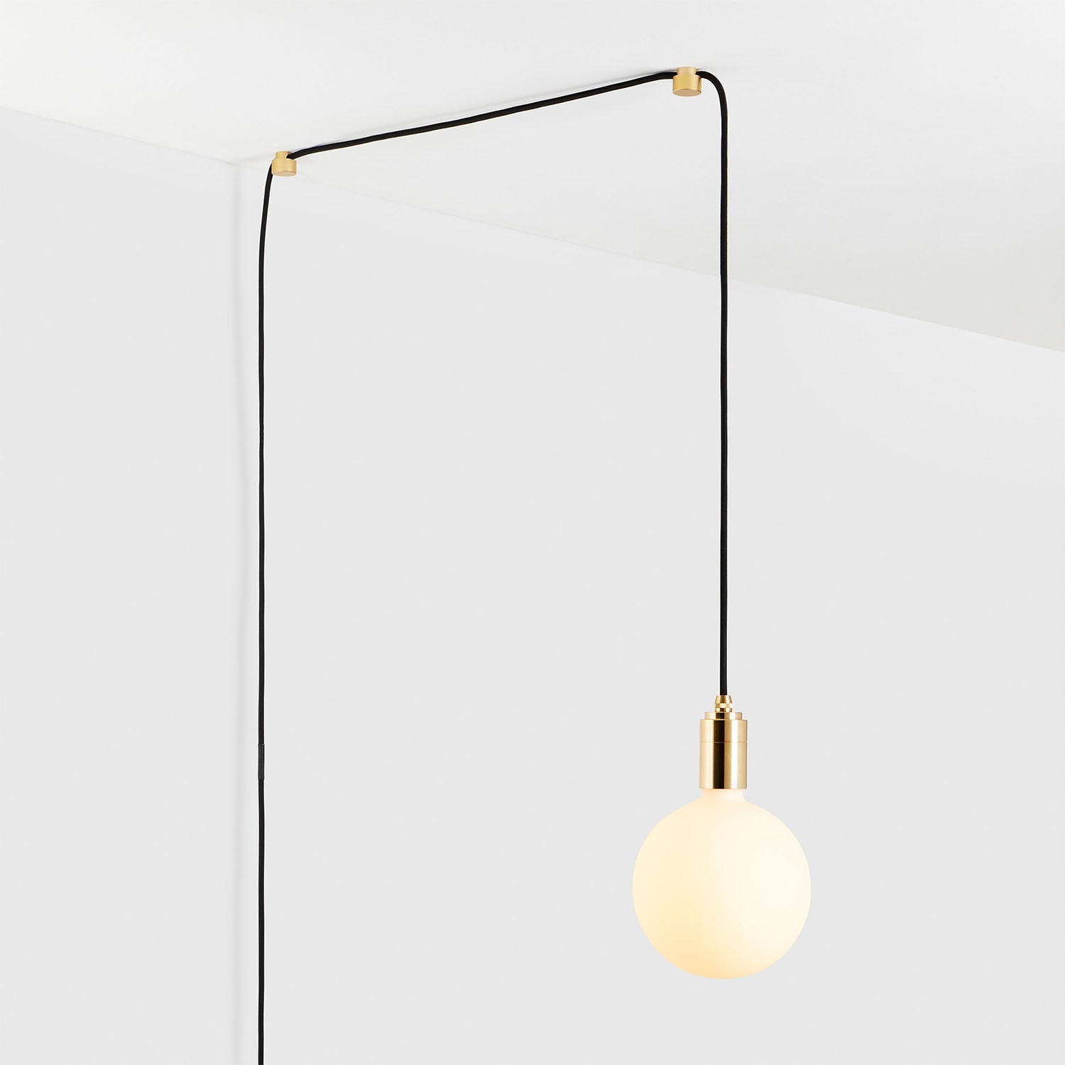 Modern hanging light fixture with a round bulb and black cord in a minimalistic white room.