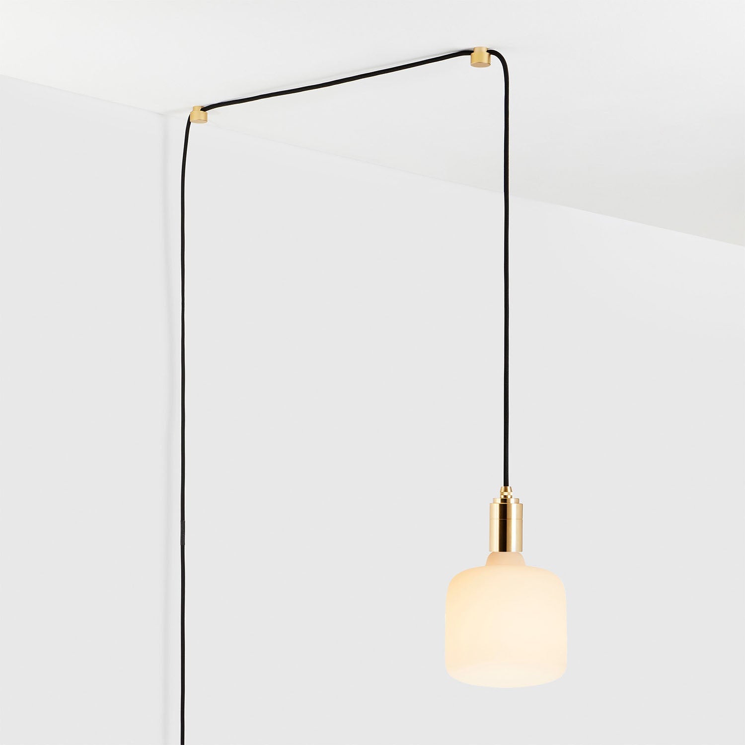Minimalist pendant light with gold fixture and black cord hanging from ceiling against white background