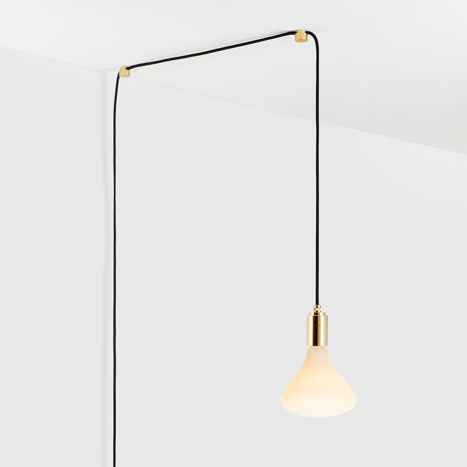 Modern minimalist pendant light with black cord and brass fixture hanging from the ceiling against a white background.