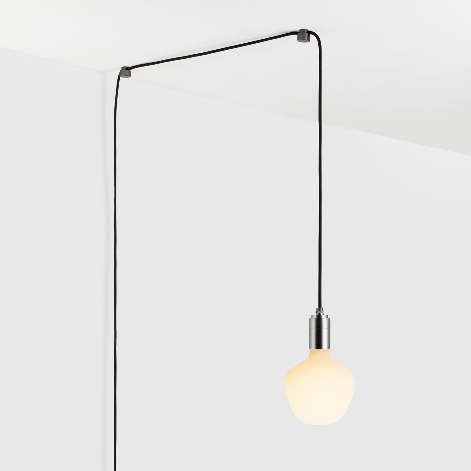 Modern hanging light bulb with black cord against a white wall and ceiling.